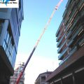 Gr�a m�vil autopropulsada telesc�pica  con plum�n de 60 metros de altura, realizando trabajos de suministro de material para reparaci�n de cubierta en edificio en el centro de Tortosa, Tarragona.